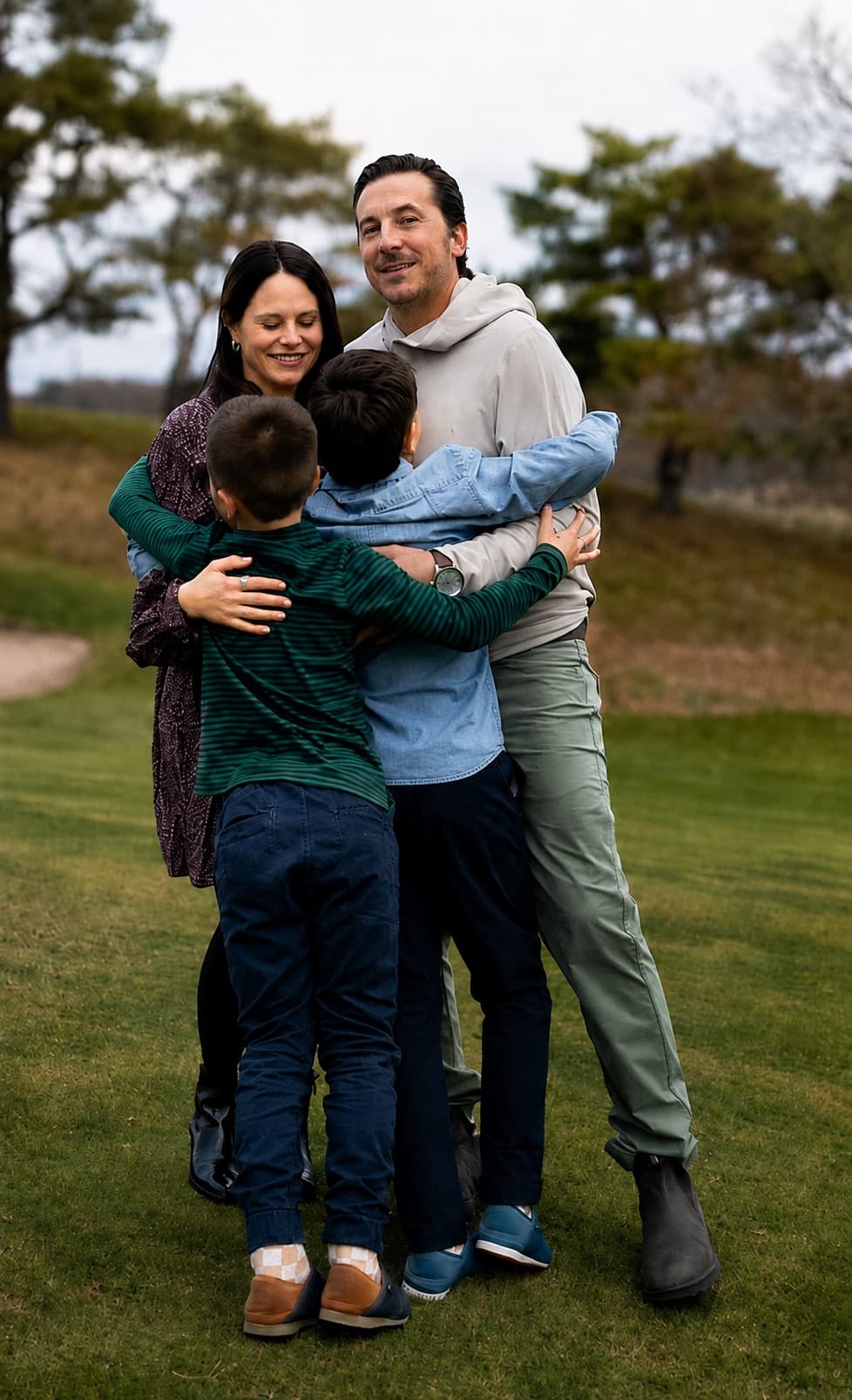 Kenzie and her husband holding Tate and Grant in a group hug outdoors.